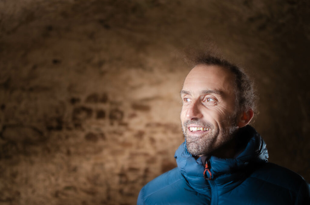 Yvain Lucas dans une grotte avec un sourire chaleureux, il regarde vers la lumière.