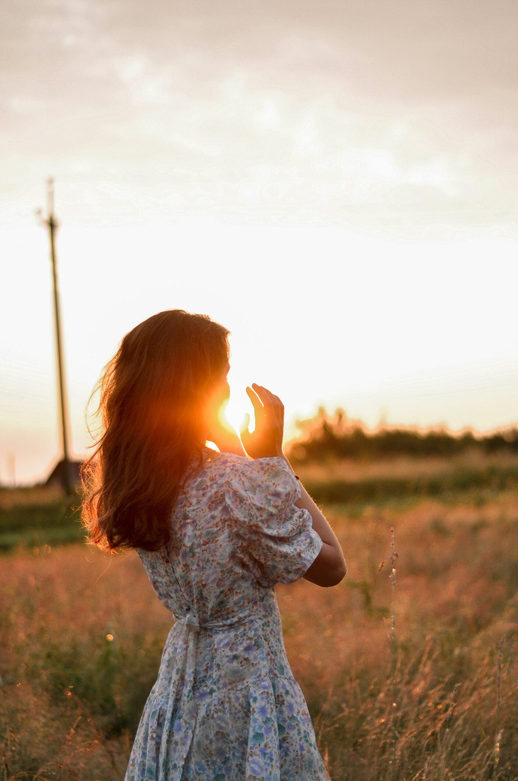 Femme en robe légère jouant avec le soleil levant entre ses mains, dans un champ d'herbes sauvages