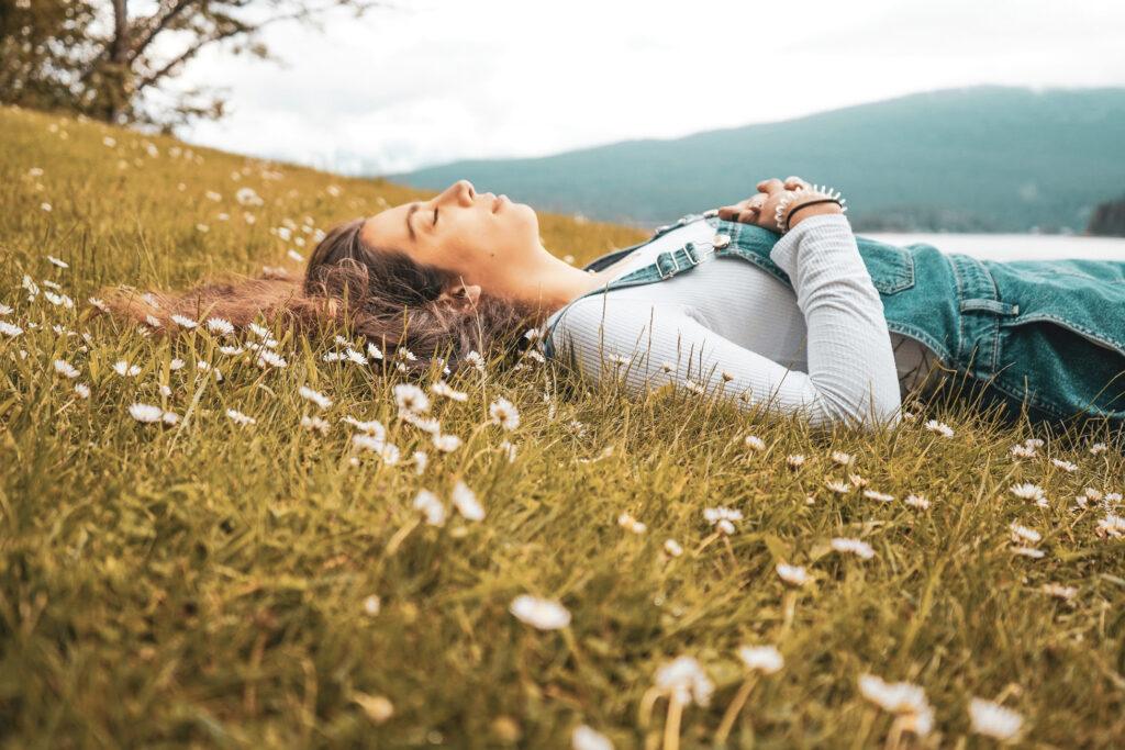 Femme paisiblement allongée dans un champ fleuri en montagne, ses cheveux se confondent avec l’environnement.